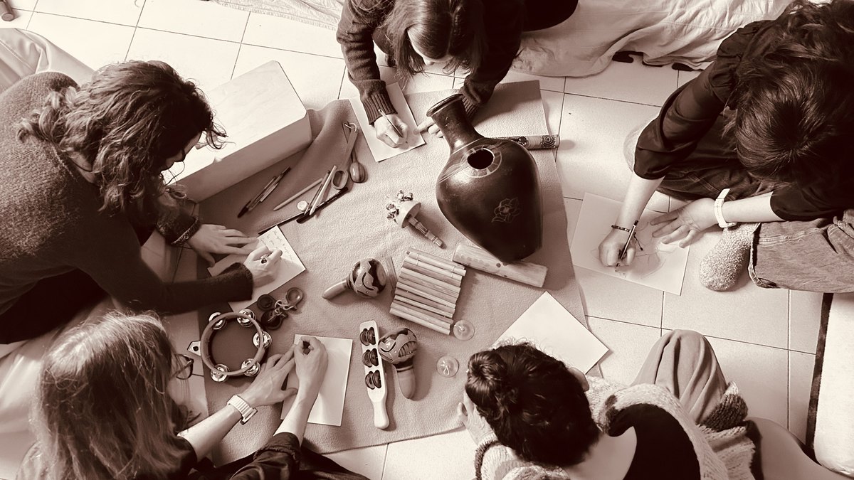 Vista cenital en tono sepia de un grupo de personas dibujando alrededor de instrumentos durante una celebración colectiva