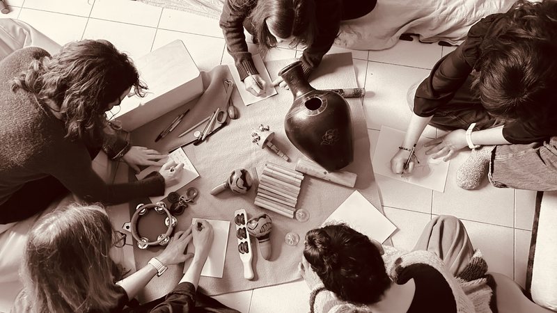 Sesión colectiva en tono sepia, personas dibujando alrededor de instrumentos