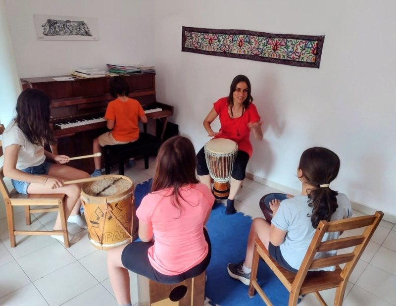 María tocando el djembé mientras cuatro peques tocan el piano y otros instrumentos