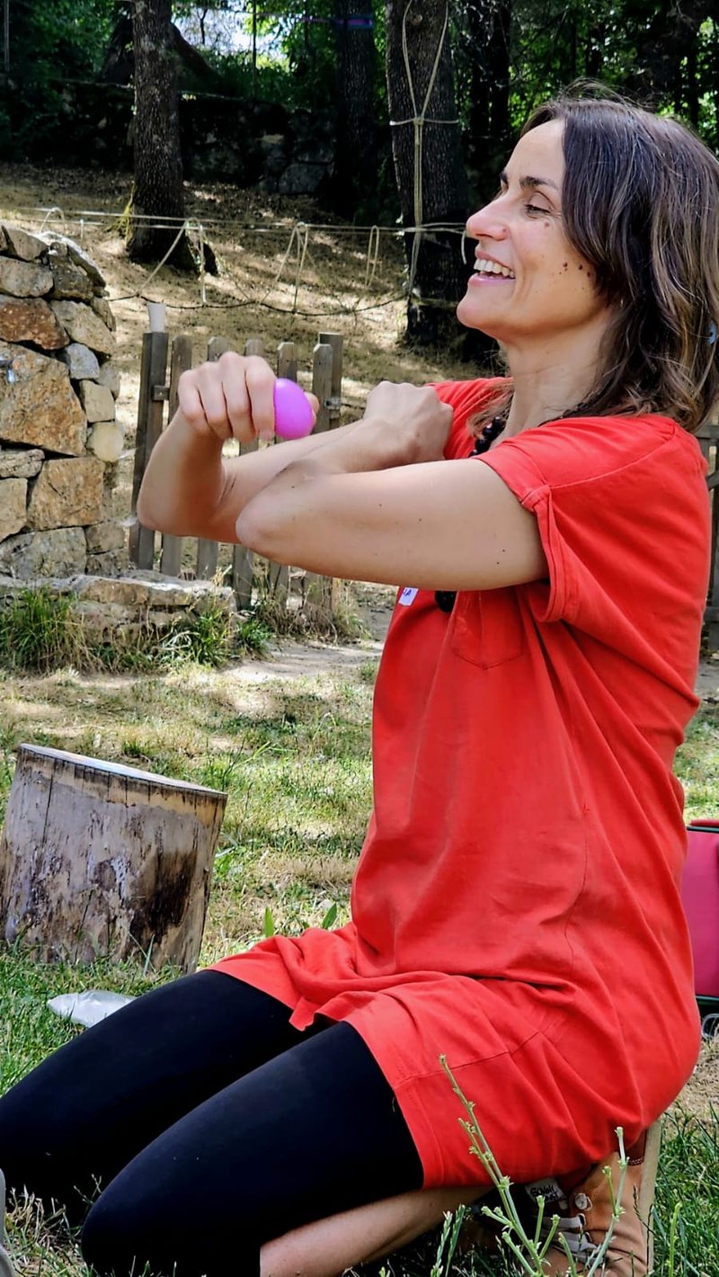 Retrato de María Moíño sonriendo con una maraca en la mano, sentada al aire libre en un jardín