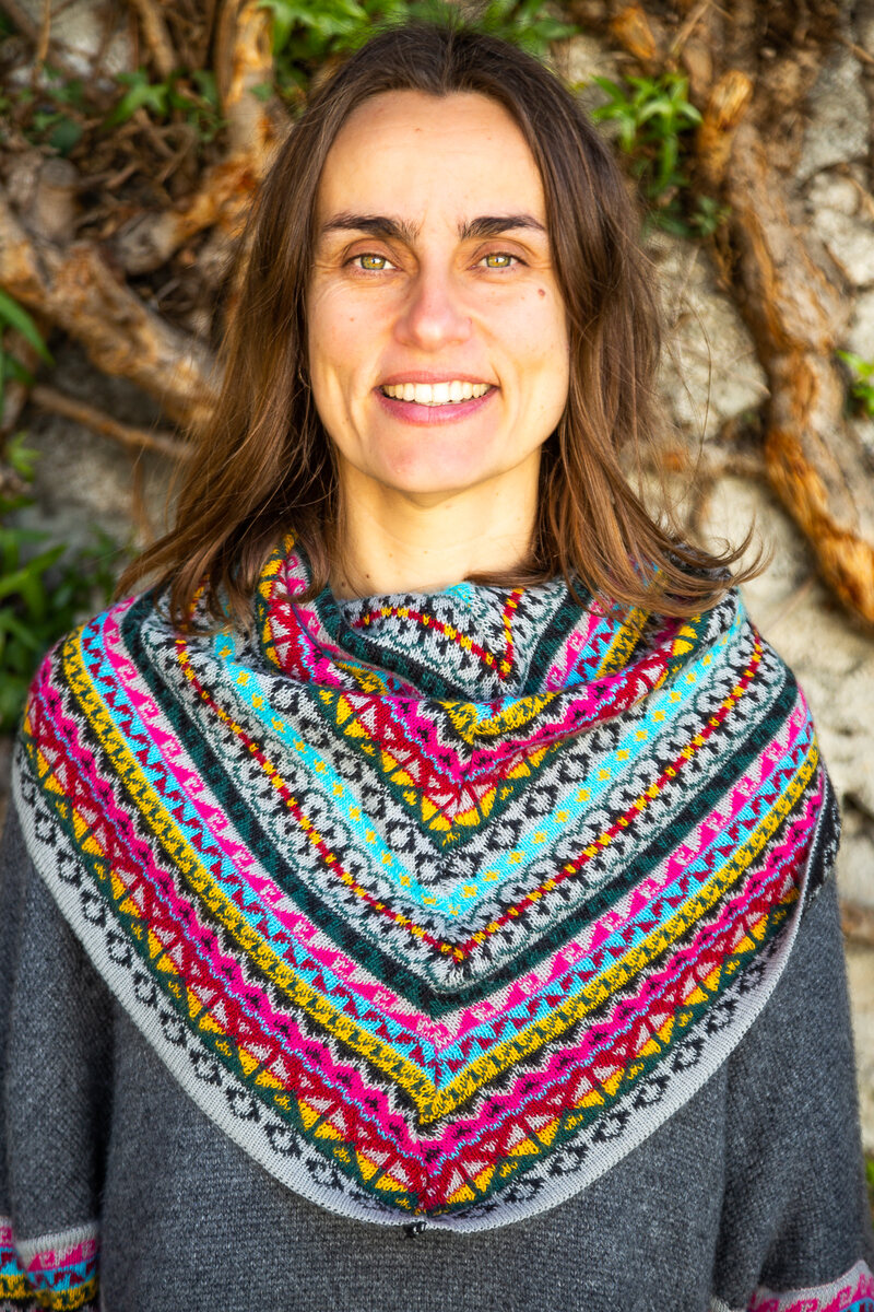 Retrato de María con un poncho tejido de colores frente a un tronco