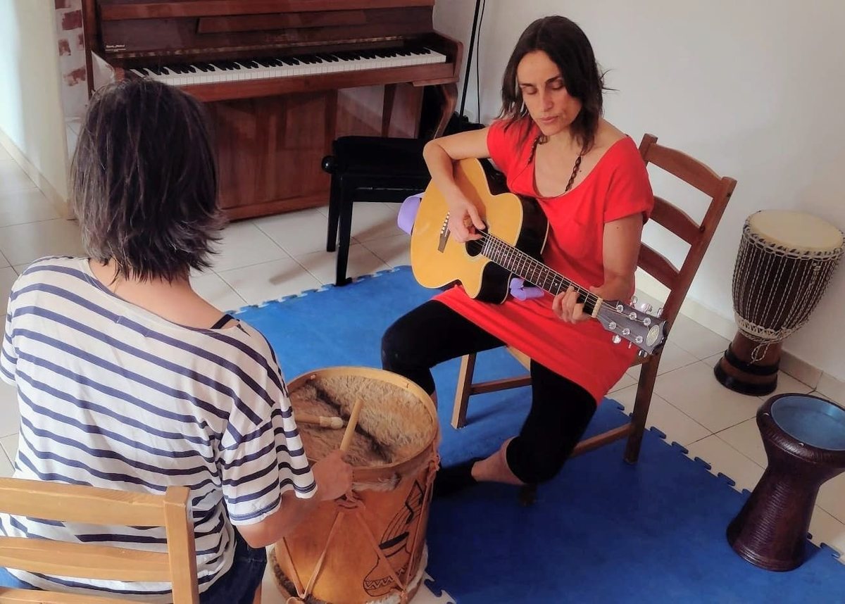 María tocando la guitarra frente a una persona adulta que toca el tambor durante una sesión de musicoterapia