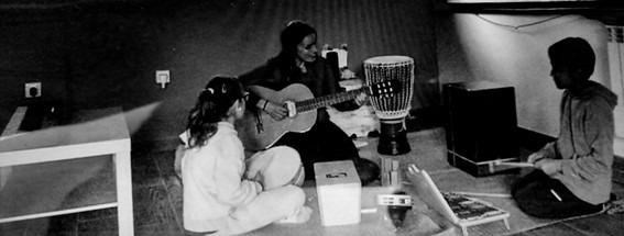 Sesión de musicoterapia en blanco y negro: María tocando la guitarra sentada en el suelo entre dos personas más