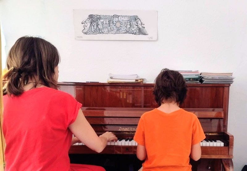 María acompañando a un peque de espaldas al piano durante una sesión de musicoterapia